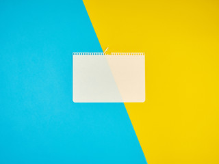 Wall Mural - blank white sheet of paper torn from a notebook on a blue-yellow background