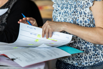 Wall Mural - Atmosphere during corporate conference. A close up view on a professional woman reading paperwork, she uses hands to check through sheets of highlighted information during an assembly.