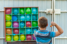 A Boy Plays Balloon Darts In The Backyard - A Box Or Set With Colorful Balloons For A Carnival Dart Game, One Ballon Popped