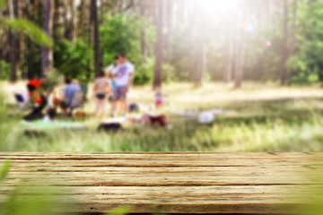 Table background with wooden top board with nice forest and gardens view in distance. Happy barbecue or picnic time with family. Empty space on the table top for an advertising product..