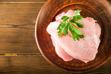 Meat fillet in a plate with rosemary, peppercorns close-up. Chicken, turkey, pork, beef fillet in a plate on a textured wooden table, copy space.