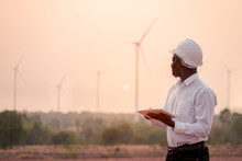 African Engineer Wearing White Hard Hat Standing With Digital Tablet Against Wind Turbine