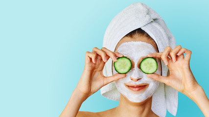 Wall Mural - beautiful young woman with facial mask on her face holding slices of cucumber. skin care and treatme