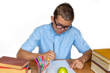 Joyful teen boy sitting at the table with pencils and textbooks. Happy pupil doing homework at the table.