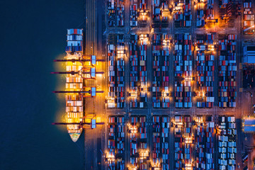 Aerial top view of container cargo ship in the export and import business and logistics international goods in urban city. Shipping to the harbor by crane in Victoria Harbour, Hong Kong City at night.