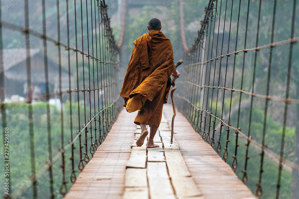 monk is walking on a wooden bridge. - obrazy, fototapety, plakaty 