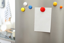 Empty Sheet Of Paper With Colorful Magnets On Refrigerator Door In Kitchen. Space For Text