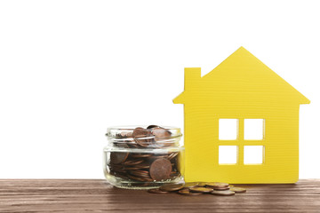 Model of house and jar with coins on table against white background. Space for text