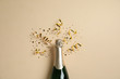 Leinwandbild Motiv Bottle of champagne with gold glitter and confetti on beige background, flat lay. Hilarious celebration
