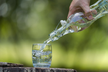 Wall Mural - Hand pouring drink water from bottle into glass with natural background