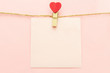 Pink blank paper sheet on a clothes line and clothespegs with red heart on a pink background. Valentines day concept