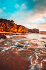 Canvas Print - Waves washing over rocks at beach with cliffs in background