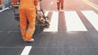 Road workers with thermoplastic spray road marking machine working to paint pedestrian crosswalk on asphalt road surface in the city