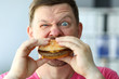 Funny bearded man with idiot facial expression eating big burger