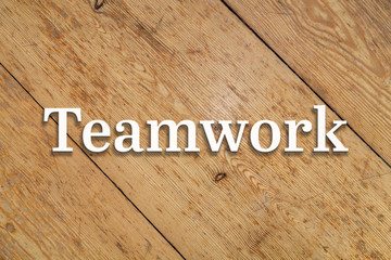 Wall Mural - `teamwork` white text on a wooden home background.
