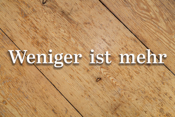 Wall Mural - `weniger ist mehr` white text on a wooden background. translation: `less is more`