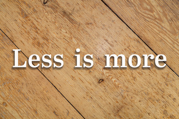 Wall Mural - `less is more` white text on a wooden home background.