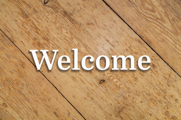 Wall Mural - `welcome` white text on a wooden background.