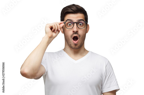Young man shouting OMG with open mouth, surprised by low price and sales, holding glasses, isolated on white background