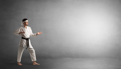 Wall Mural - Small karate man fighting in an empty grey copy space