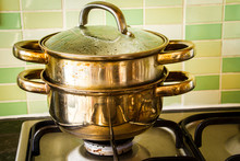 Old And Rusted Stainless Steel Steamer On A Gas Hob With Green Tiles In The Background