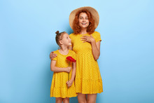 Lovely Small Girl In Yellow Polkadot Summer Dress Gives Red Gerbera Flower To Her Mom, Receives Warm Hug. Touched Red Haired Beautiful Mother Gets Favourite Flower From Daughter On Birthday.