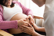 © InfiniteFlow - Pregnant couple of husband and wife feels love and relax at home. Young expecting woman holds baby in pregnant belly. Father take care of pregnant mother. Concept of maternity and pregnancy care.