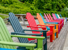 Colorful Wood Adirondack Chairs Lined Up On A Dock Overlooking A River