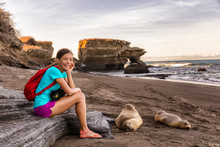 Portrait Of Woman Tourist Smiling Happy Looking At Camera On Galapagos Islands Sitting By Sea Lions On Galapagos Adventure Travel With Cruise Ship, Puerto Egas (Egas Port) Santiago Island, Ecuador.