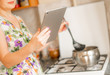 © Mihail - housewife woman holding a gadget smartphone or tablet to check receipt while cooking at the kitchen