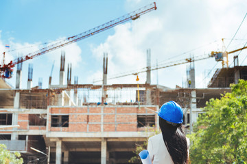 Asian woman architect wearing blue safety helmet checking working progress at contruction site.