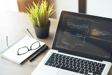 wood programmer office desk table with laptop with the software code displaying on it.