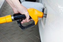 A Man's Hand Holds A Filling Gun Inserted Into The Hole Of A Gasoline Tank Of A Car On A Gasoline Fueling. Close-up Of The Hand And Fuel Filling Pistol. Yellow Refueling Gun At The Refuel Station.
