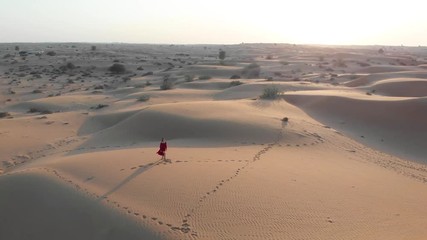 Wall Mural - Woman walking in the desert at sunset aerial