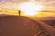 © Jantira - Photographer behind tripod standing with camera on sand dune silhouetted by sunrise in desert, Death Valley California
