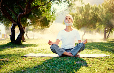 Wall Mural - Yoga at park. Senior bearded man in lotus pose sitting on green grass. Concept of calm and meditation.