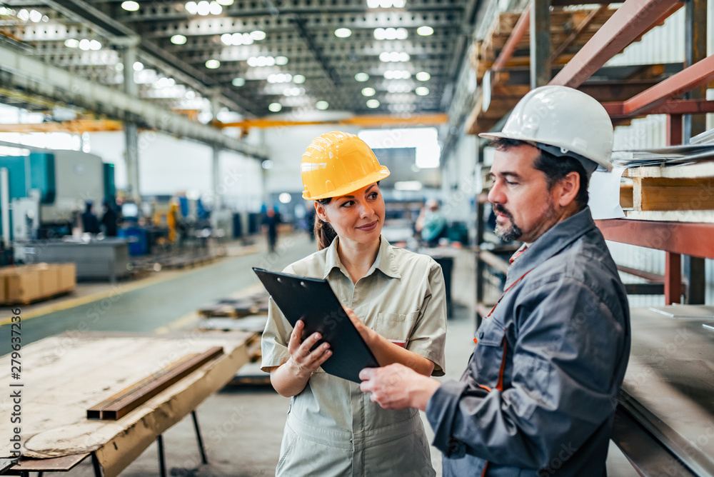 Factory worker and female manager discussing about work in metal industry factory. - obrazy, fototapety, plakaty 