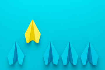 Top view of yellow paper plane as out of the crowd concept over turquoise blue background with copy space. Flat lay image of paper plenes as leadership concept. Leaving the crowd metaphor.