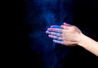 Blue powder splatted from woman hands on black background