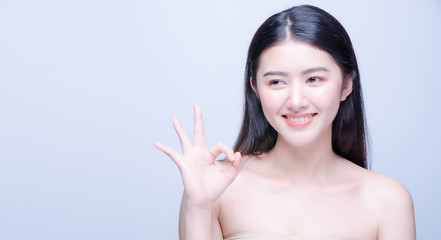 Beauty portrait of a cheerful attractive half naked asian woman showing ok gesture and looking forward at camera isolated over bright blue background.