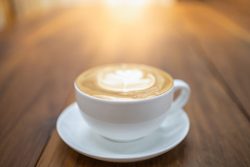 Close up of white cup of hot coffee latte with milk foam art on wooden table and copy space.