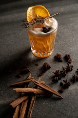 Canvas Print - Vertical shot of a cocktail with an orange slice and dry herbs near a cinnamon sticks