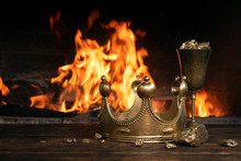 Golden Crown And A Goblet Full Of Gold On The King Table Over Burning Fire Background.