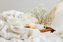 Wooden Tray Of Coffee And Candles With Flowers On Bed. White Bedding Sheets With Striped Blanket And Pillow. Breakfast In Bed. Hygge Concept.
