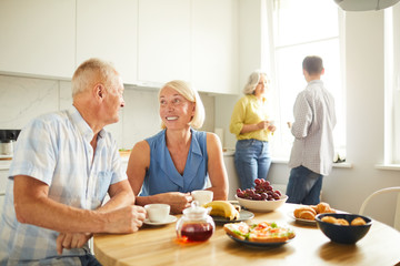 Wall Mural - Portrait of happy mature couple looking at each other tenderly while siting at kitchen table in sunlight, copy space