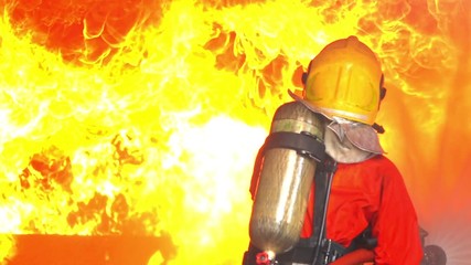 Wall Mural - FHD 250 fps slow motion medium shot of firefighter in fire suit during fire extinguishment fighting a fire by using a hose and water in burning building. Emergency services occupation safety concept.