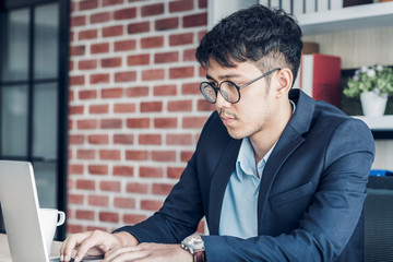 Wall Mural - Young Asian businessman wear suit working with laptop on desk table in modern office.connecting network online concept