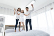 © xreflex - Asian family happy on the bedroom in the house with sunlight from the window. Father, mother and daughter, aged three, jumping on the bed, playing and laughing