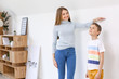 © Pixel-Shot - Mother measuring height of her son near wall