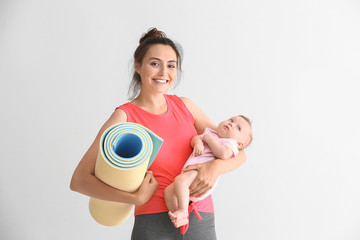 Mother with yoga mat and cute little baby on white background